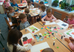 Dzieci przy stolikach komponują pojazdy z kolorowych figur geometrycznych.